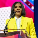 A woman in a yellow blazer speaking at a podium with a microphone