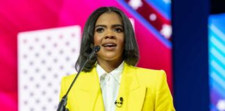 A woman in a yellow blazer speaking at a podium with a microphone