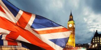 Union Jack flag waving with clock tower in London at dusk