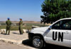 UN peacekeepers stand near a white UN vehicle overlooking rural landscape