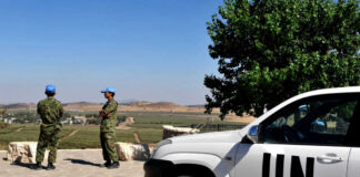 UN peacekeepers stand near a white UN vehicle overlooking rural landscape