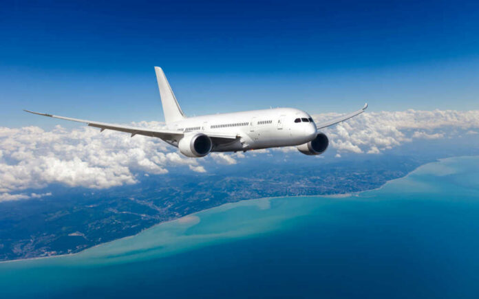 Airplane flying over coastline and clouds in sky