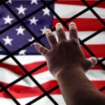 Hand reaching through fence toward American flag
