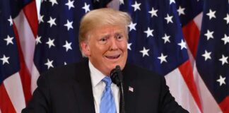 man at podium with U.S. flags behind him