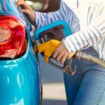 Person refueling a blue car with a yellow gas nozzle
