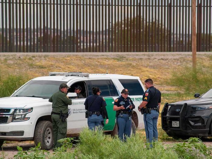 law enforcement officers confer beside patrol vehicles near a border fence