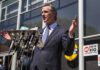 man in suit speaking at outdoor press conference