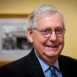 elderly man wearing glasses and a suit smiling