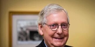 elderly man wearing glasses and a suit smiling