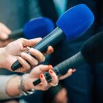 Airport Uproar Greets Trump Touchdown Reporters holding colorful microphones