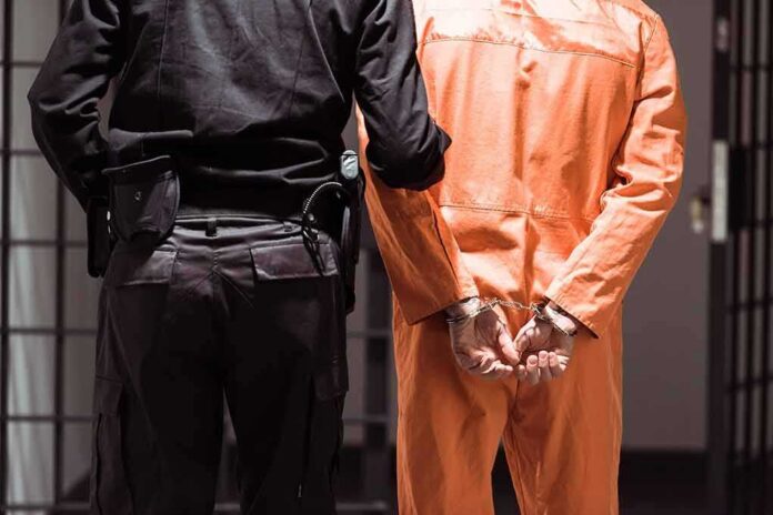 shutterstock_1030213828 Prisoner in orange jumpsuit handcuffed with guard standing beside