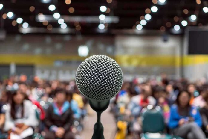 shutterstock_1079876627 Microphone on stage facing a blurred audience