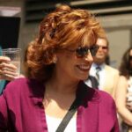 Graphic Jab Airs – Trump Name Invoked Woman in sunglasses holding a plastic cup and smiling outdoors