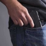 Hand placing a handgun into a jeans pocket