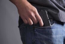 Hand placing a handgun into a jeans pocket