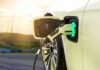Electric car charging with a plugged-in connector at sunset