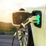 Beijing’s Auto Gambit Rattles Big Oil Electric car charging with a plugged-in connector at sunset