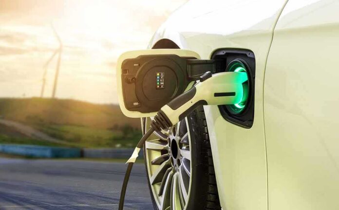 shutterstock_1179686422 Electric car charging with a plugged-in connector at sunset