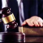 Judge's gavel striking block with hand on book in background