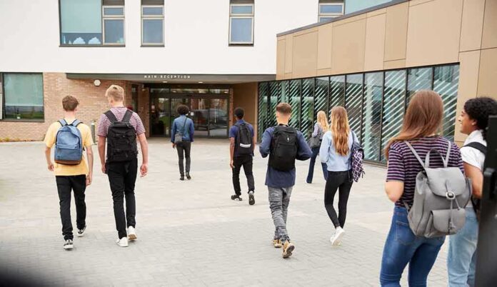 shutterstock_1188882382-1 Students with backpacks walking toward a school entrance