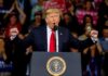 politician speaking at a rally with raised fists behind a podium