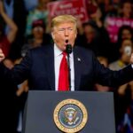 politician speaking at a rally with raised fists behind a podium
