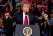politician speaking at a rally with raised fists behind a podium