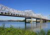 A large metal bridge spanning over a river with a clear blue sky in the background