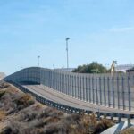 Tall metal border fence curving through arid landscape