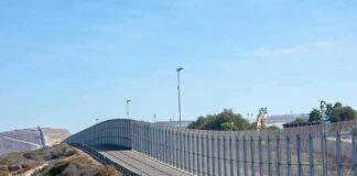 Tall metal border fence curving through arid landscape