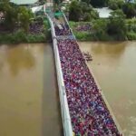 Crowd of people densely packed on a bridge over a muddy river