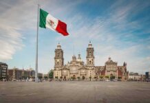 Mexican flag over a historic cathedral in a large city square