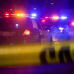 Police cars with flashing lights behind yellow caution tape at night