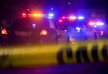 Police cars with flashing lights behind yellow caution tape at night