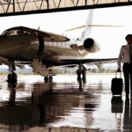 Pilot walking with suitcase beside private jet in hangar