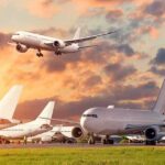 Passenger jets on airport tarmac with one aircraft landing at sunset