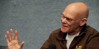 James Carville speaking into a handheld microphone, gesturing with his left hand