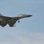 Military fighter jet in flight with landing gear down