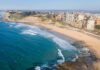 Unsafe Bluff Homes – Students Move In Anyway Aerial view of a coastal city beach with waves and rocky shoreline