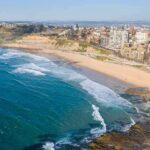 Aerial view of a coastal city beach with waves and rocky shoreline