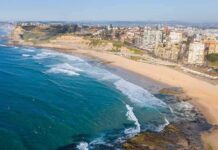Unsafe Bluff Homes – Students Move In Anyway Aerial view of a coastal city beach with waves and rocky shoreline