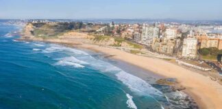 Aerial view of a coastal city beach with waves and rocky shoreline