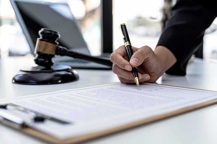 Hand signing legal document beside gavel and laptop