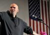 Viral Clip Chaos: Senator’s Party Slip Bald man speaking at a microphone with a U.S. flag in the background