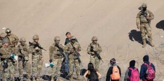Soldiers stand behind barbed wire facing civilians