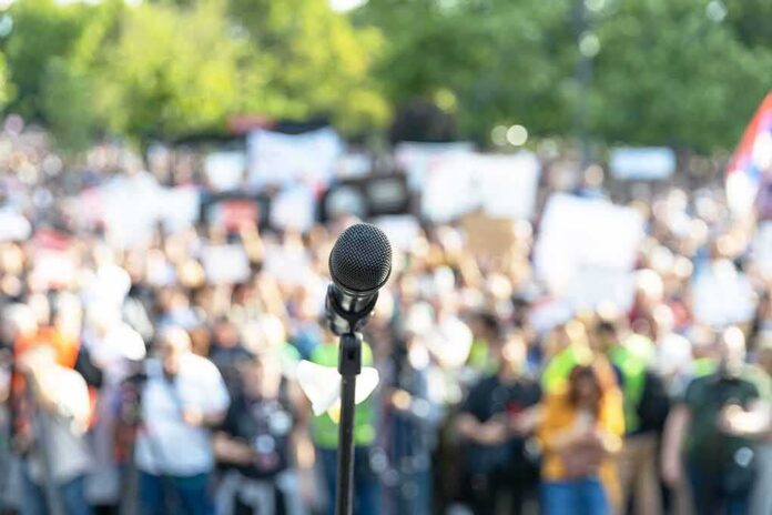 shutterstock_2313962807 Microphone on a stand facing a large blurred crowd