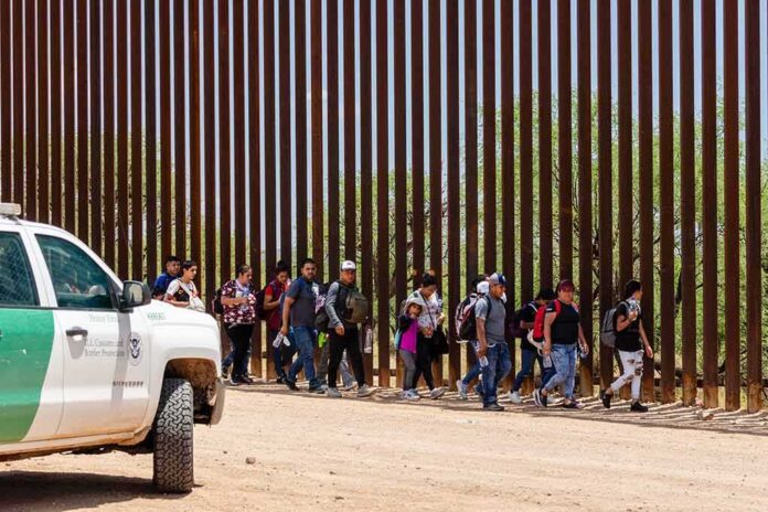 Group of people walking along a tall border fence beside a patrol vehicle