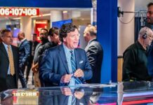 Tucker Torches Algebra – Calls It ‘Fake Math’ news anchor at a studio desk with crew and onlookers