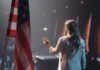 One Word Changed A Familiar Patriotic Lyric American flag and speaker at podium addressing audience