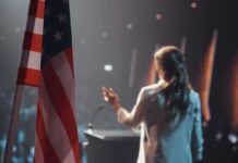One Word Changed A Familiar Patriotic Lyric American flag and speaker at podium addressing audience